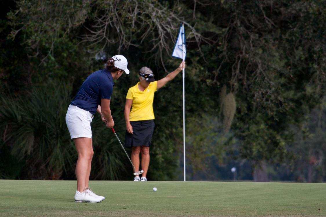 Two Women golfing. One woman putting and one holding the flag in Creve Coeur, MO where JD Hippler Real Estate is located
